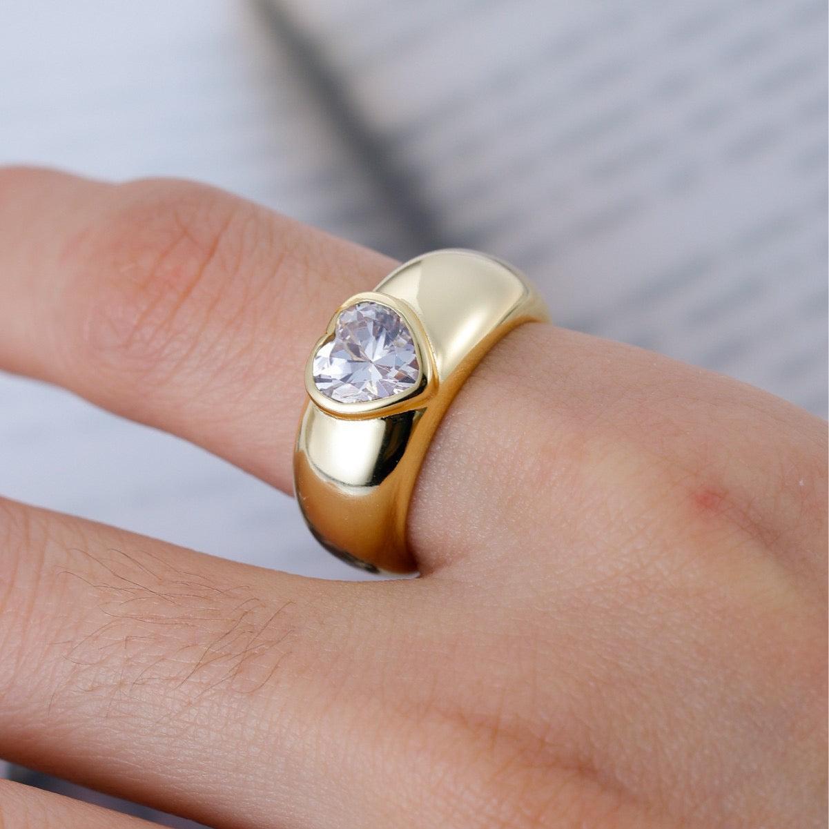 1.2ct heart-cut moissanite ring in a gold-plated dome band with a flush bezel setting on a finger.