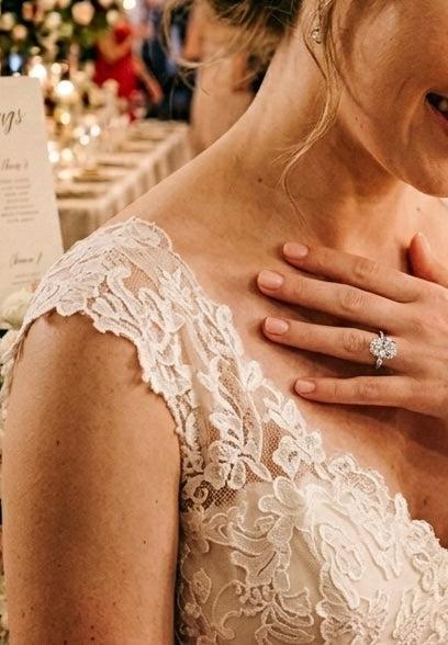 7x10mm oval moissanite solitaire ring in S925 silver with a four-prong setting worn by a bride in a lace wedding dress.