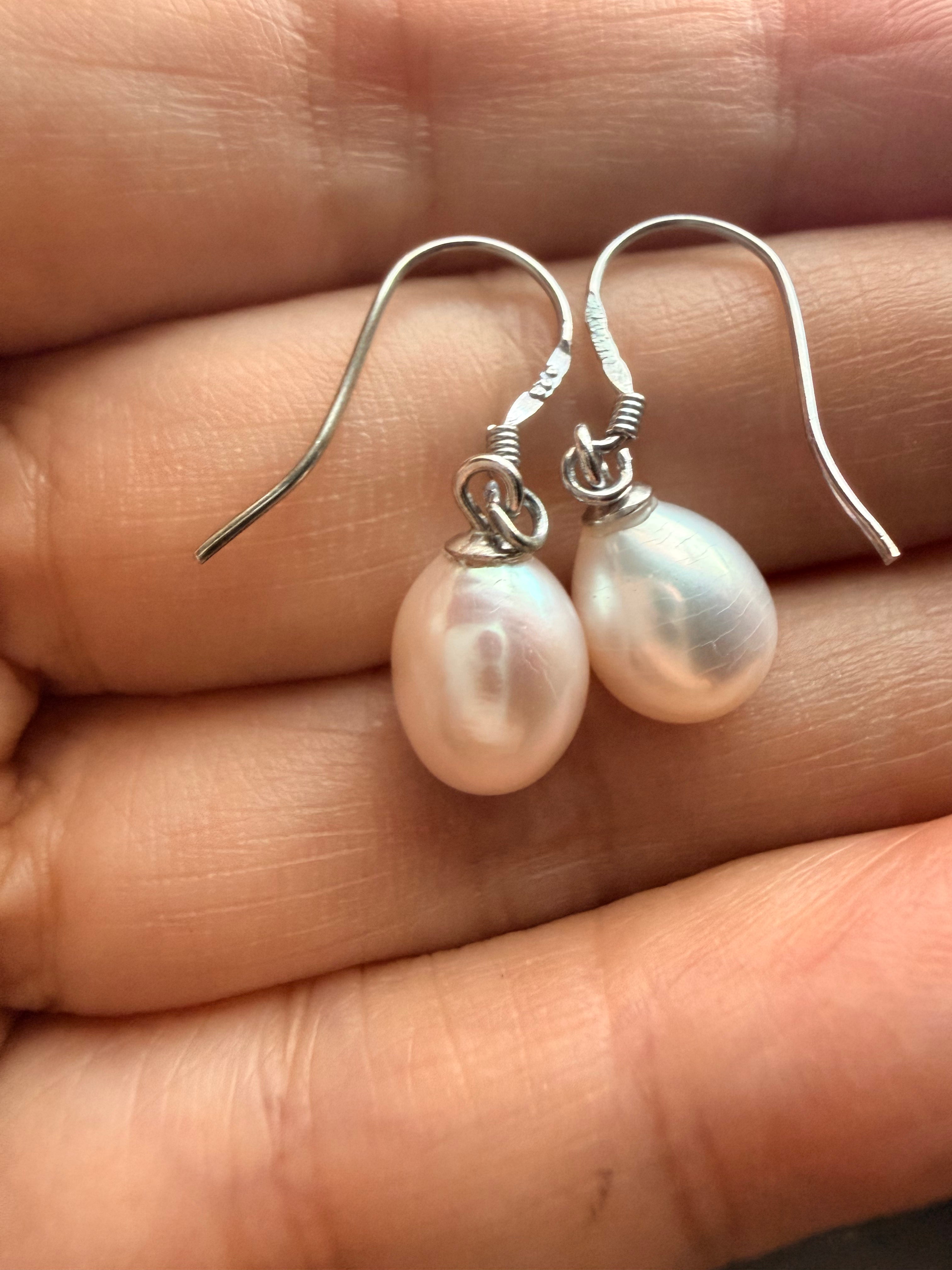 Baroque freshwater pearl drop earrings with 7-8mm white pearls on 925 sterling silver hooks held in a hand.