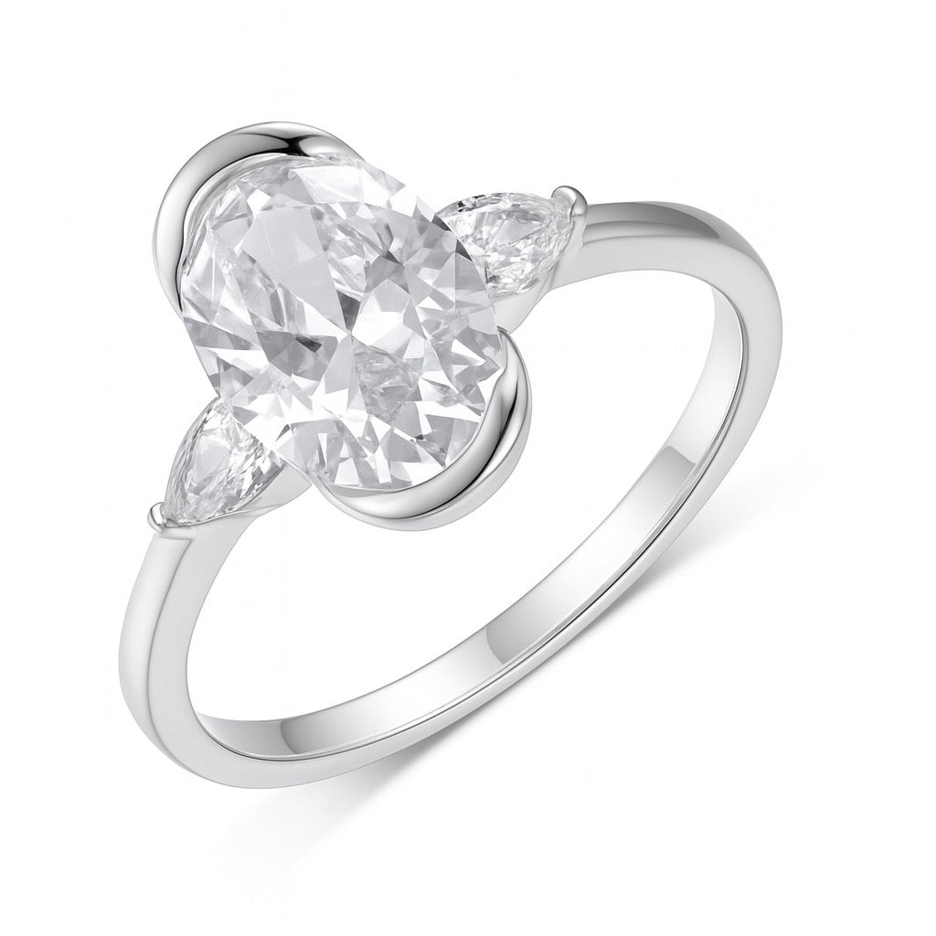 Three-stone oval moissanite ring with pear-cut side stones in a polished sterling silver half-bezel setting.