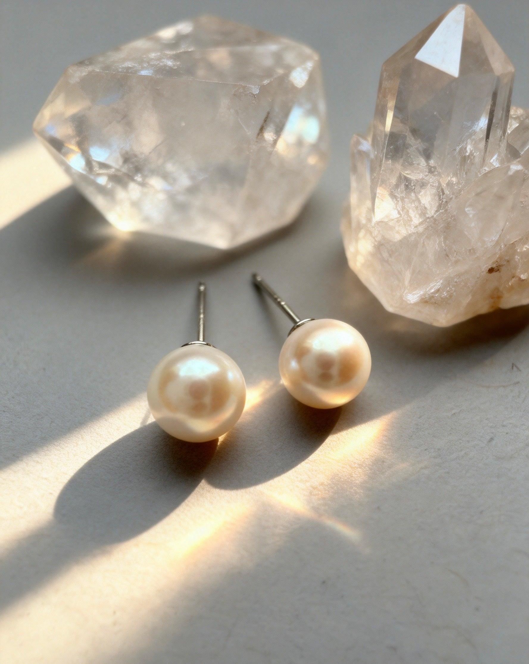 7mm round white saltwater pearl stud earrings with sterling silver posts beside clear quartz crystals.