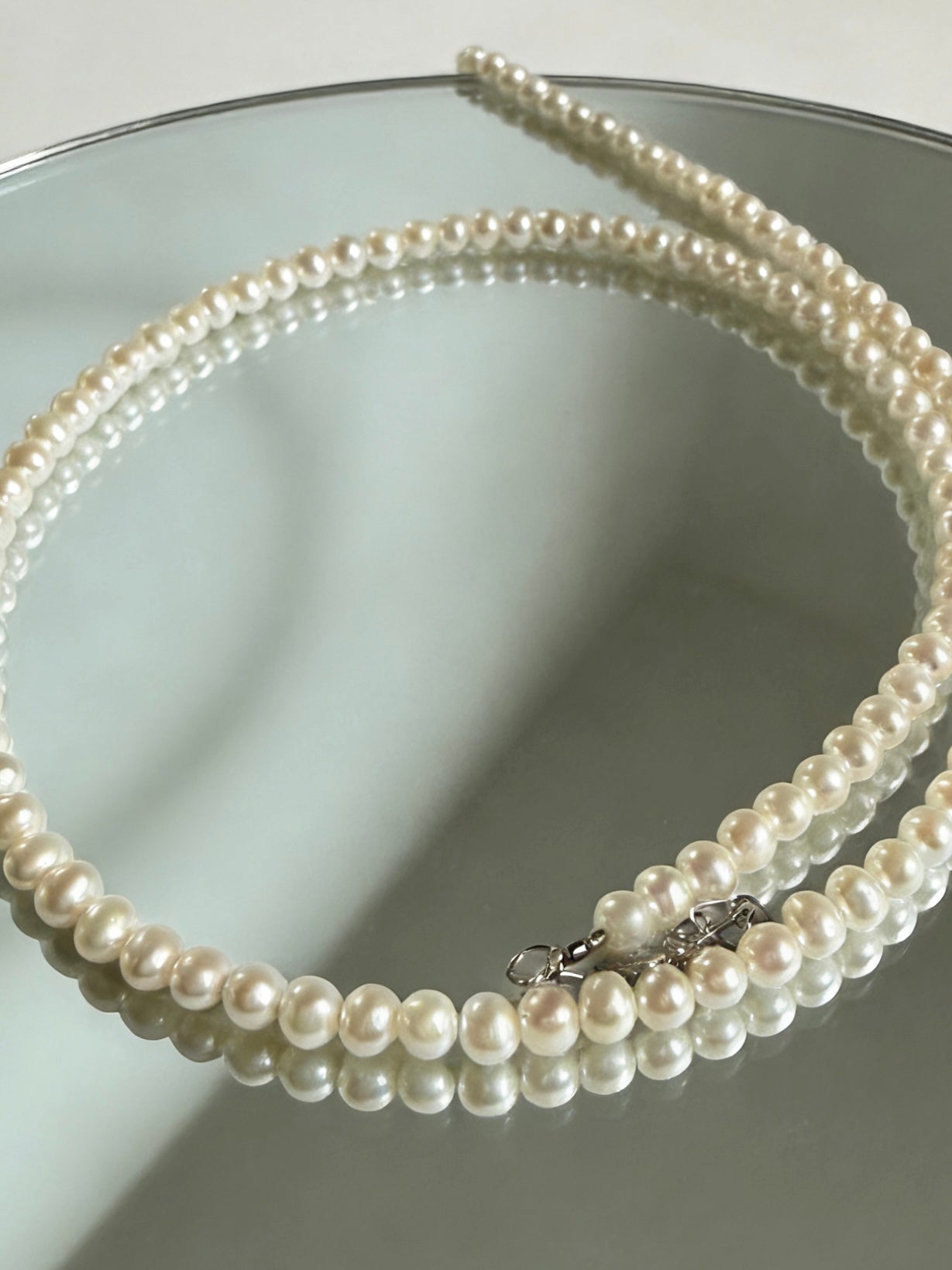 Minimalist 3–4mm white freshwater pearl choker necklace with a 925 sterling silver clasp, displayed on a reflective surface.