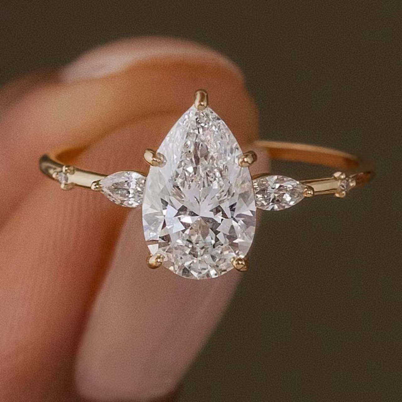 Pear-cut moissanite engagement ring with scattered marquise accent stones on a delicate gold band.