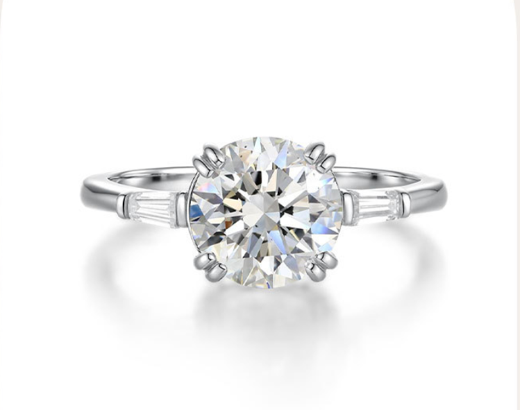 Six-prong round moissanite engagement ring in S925 silver with tapered baguette side stones on a polished band.