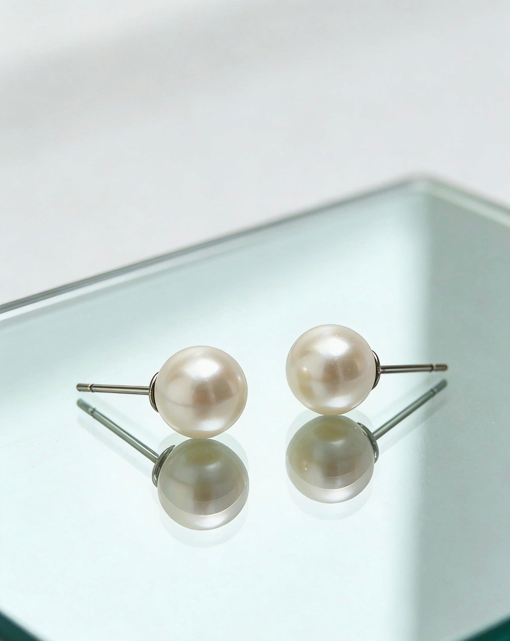 7mm white freshwater pearl stud earrings with sterling silver posts on a reflective surface.