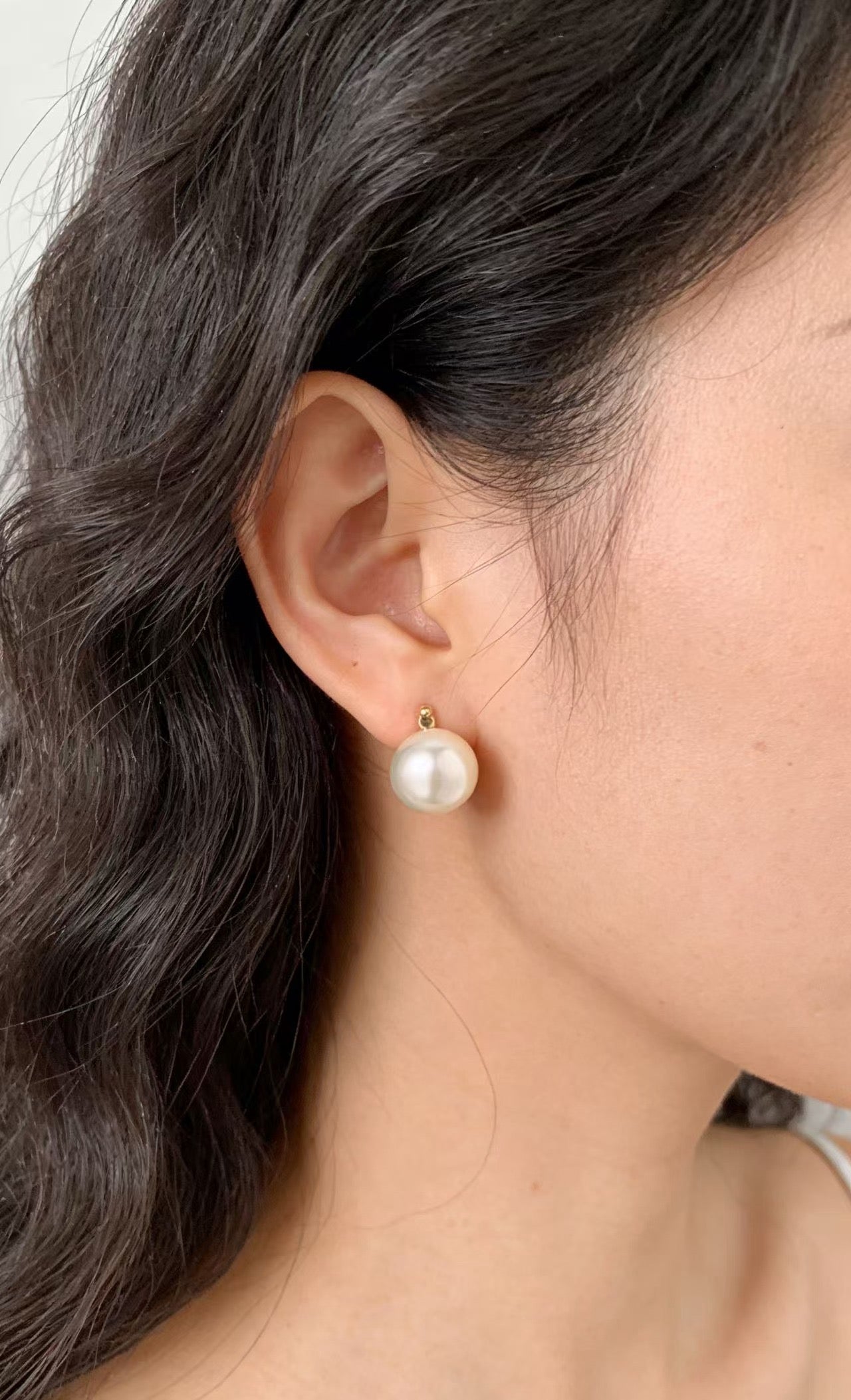 7mm round white saltwater pearl stud earring with a gold-tone setting worn on an earlobe.
