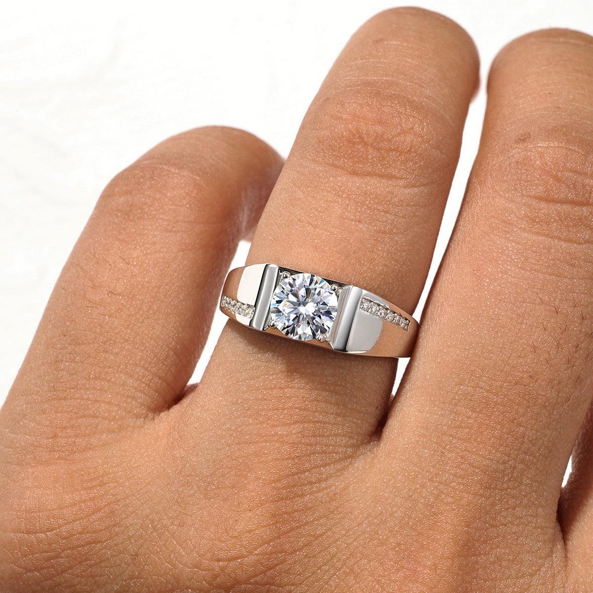 Men's 1ct round moissanite wedding ring in S925 silver with a pavé accent band worn on a finger.
