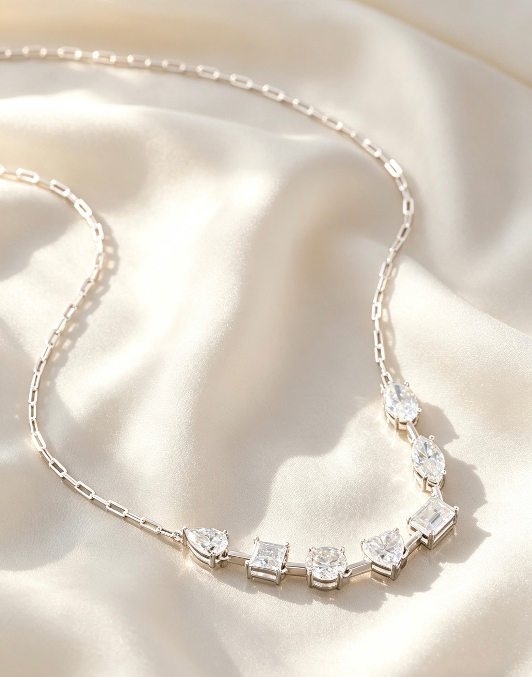 Sterling silver necklace featuring multi-shape D-color moissanite stones on a delicate chain against ivory silk.