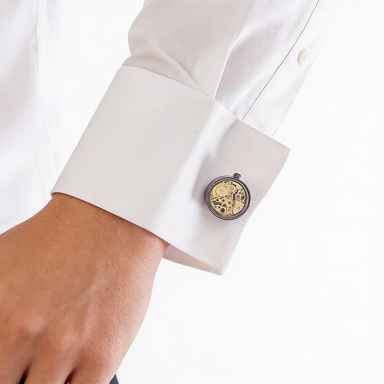 Brass skeleton movement cufflinks with visible gold gears and ruby bearings on a white dress shirt cuff.