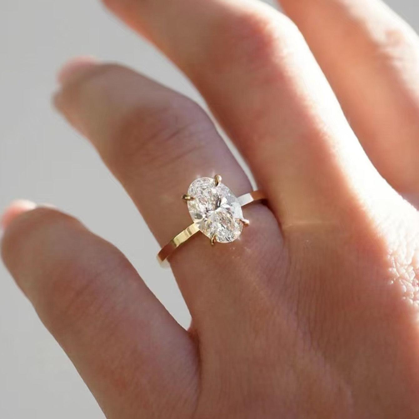 7x10mm oval moissanite solitaire ring in a gold four-prong setting worn on a finger.