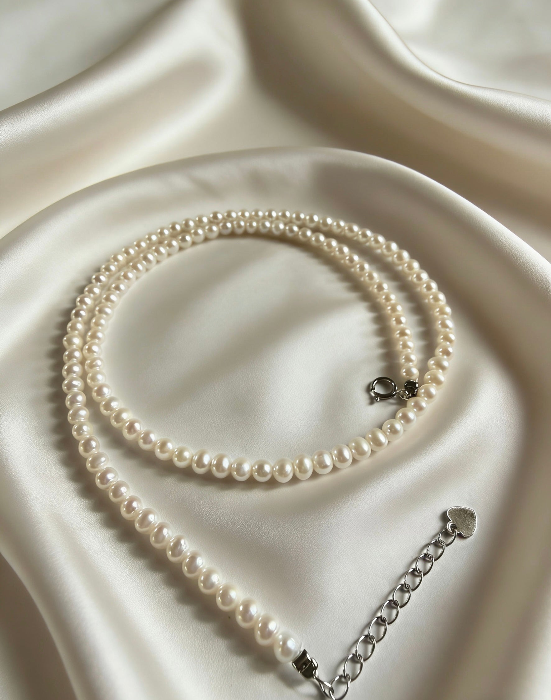 Minimalist 3–4mm white freshwater pearl choker necklace with a 925 sterling silver clasp on a soft white satin background.