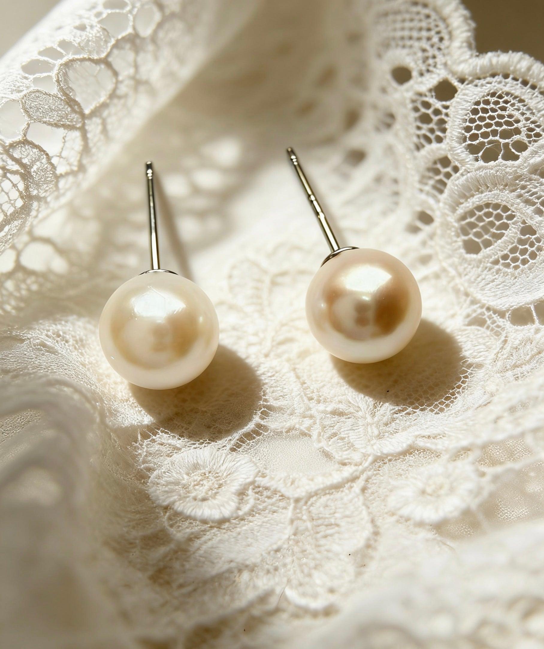 7mm round saltwater pearl stud earrings with sterling silver posts resting on delicate white lace fabric.