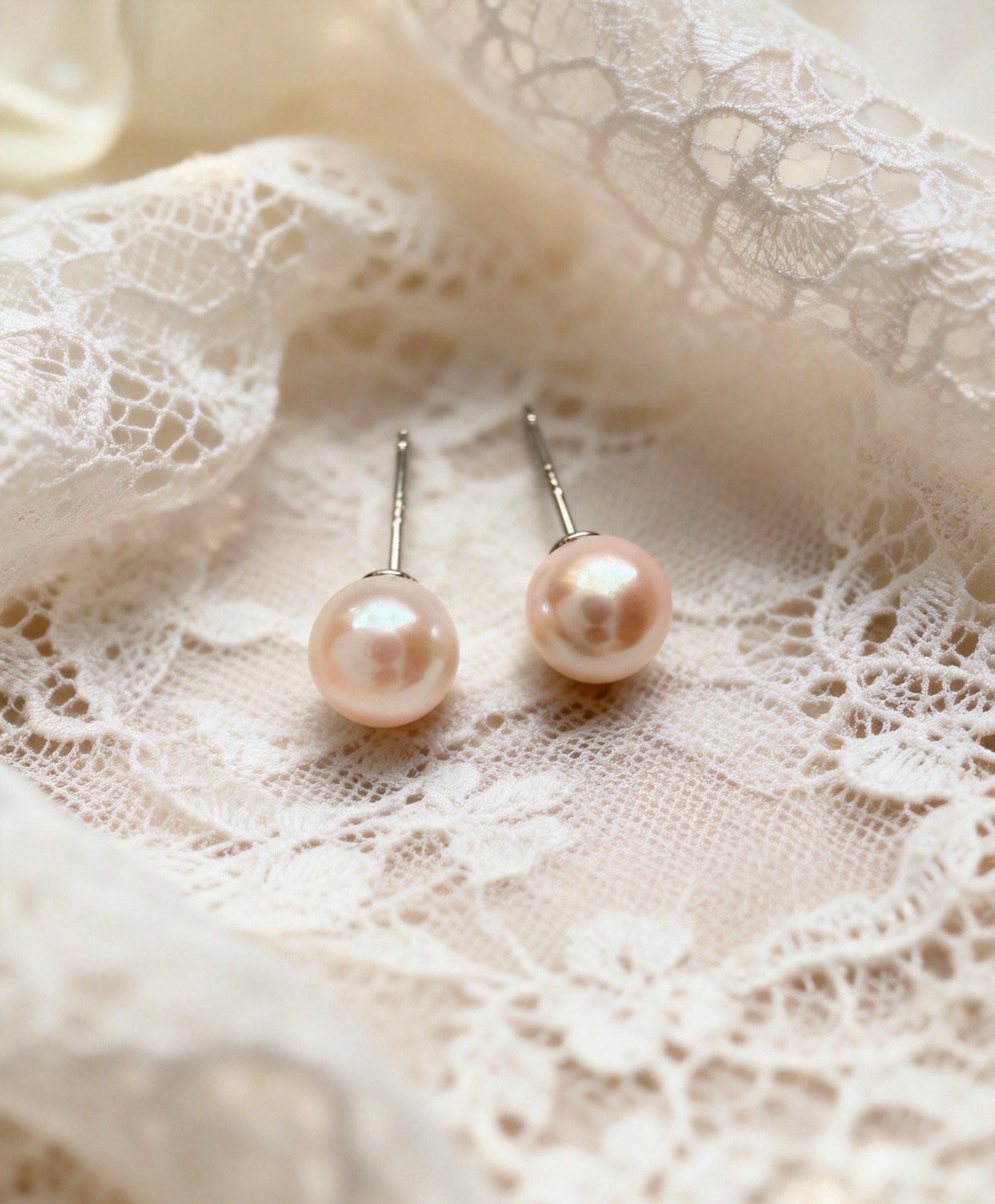7mm natural freshwater pearl stud earrings with sterling silver posts resting on delicate white lace fabric.