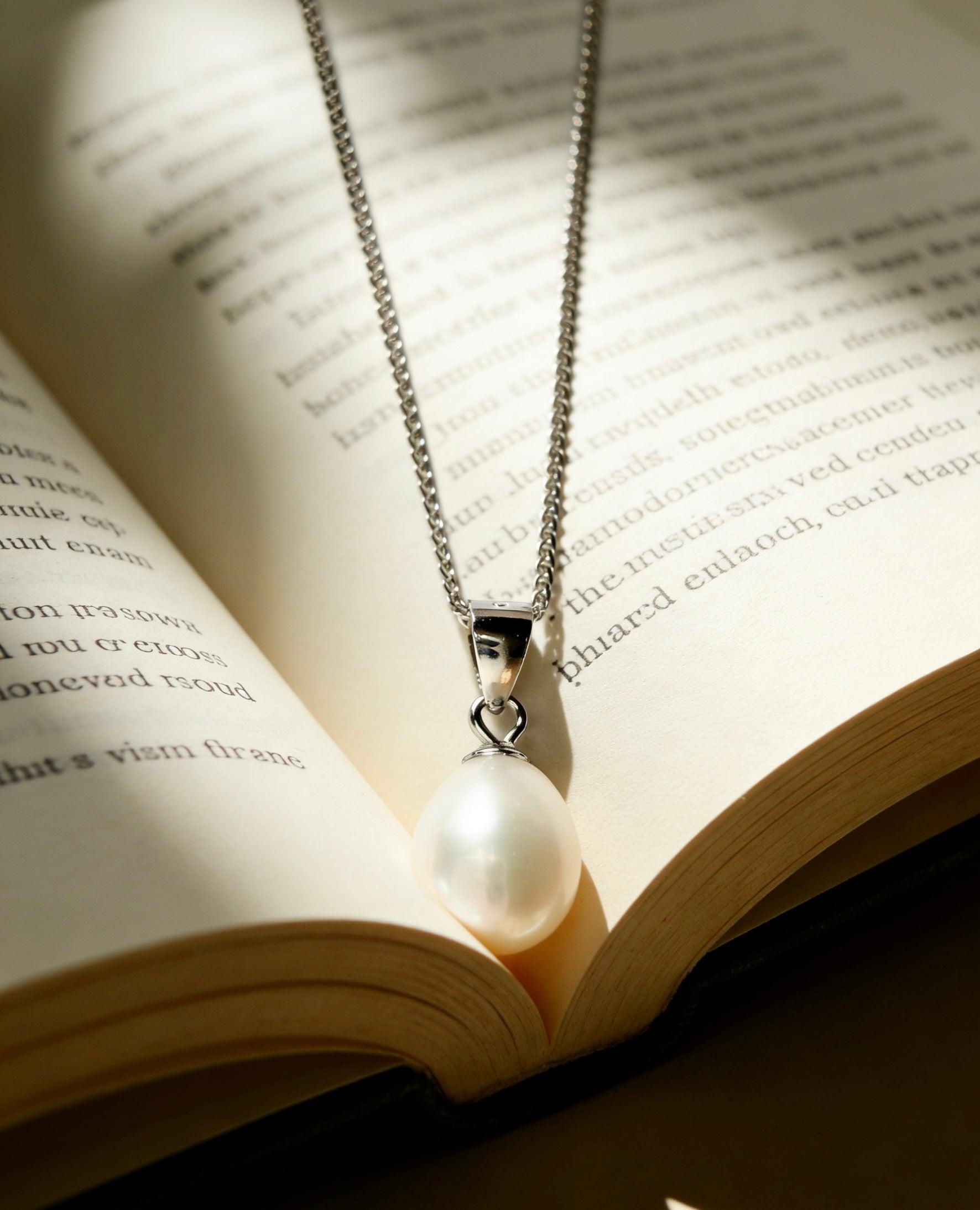 Baroque freshwater pearl pendant on a delicate 925 sterling silver chain resting on an open book.