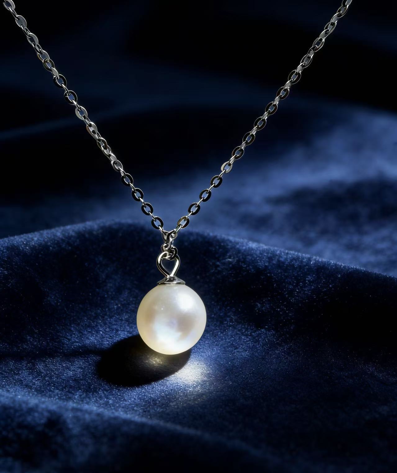 7mm round Hepu saltwater pearl pendant on a delicate silver chain against a dark blue velvet background.