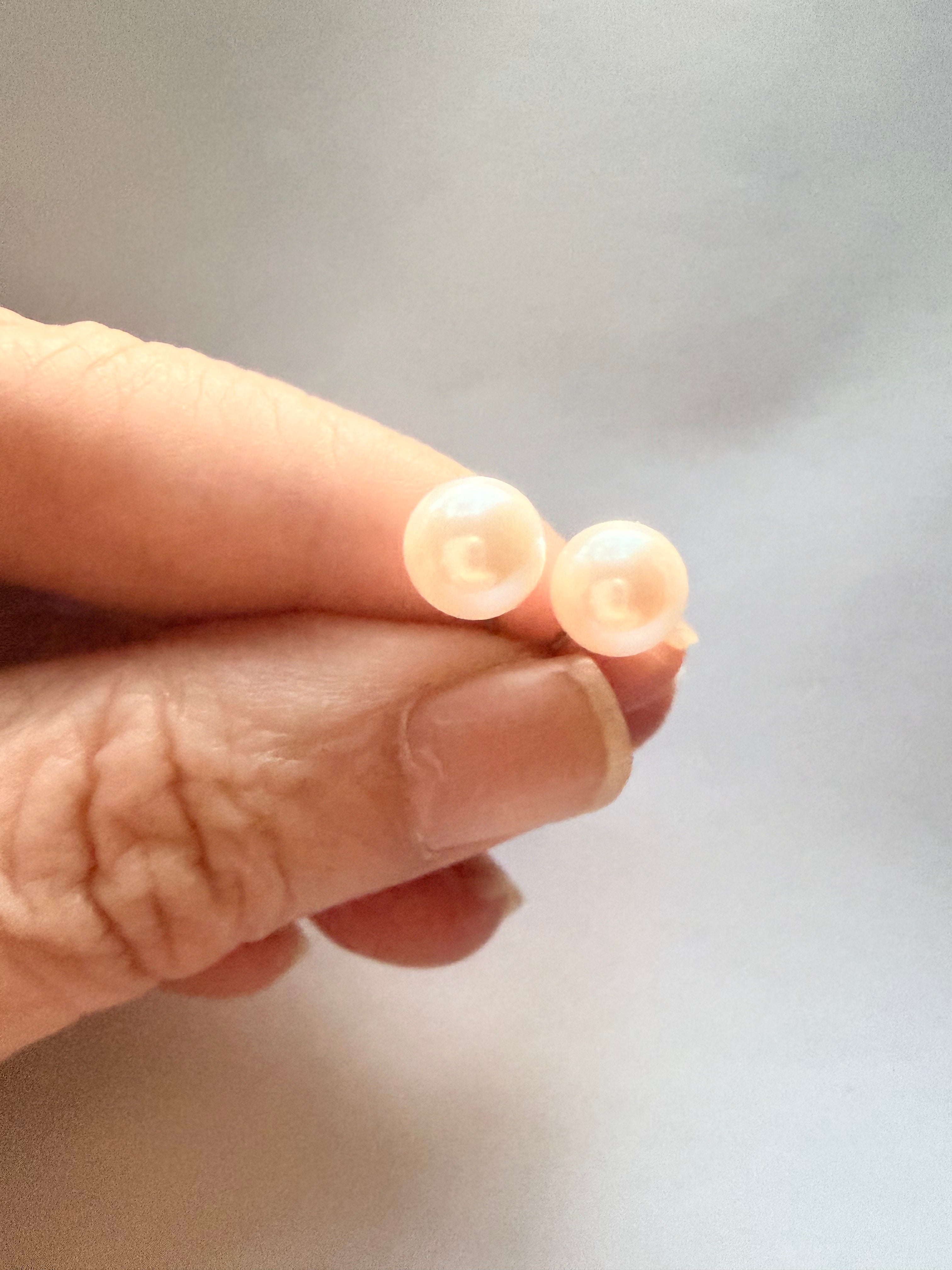 7mm natural freshwater pearl stud earrings with sterling silver posts held between fingers.
