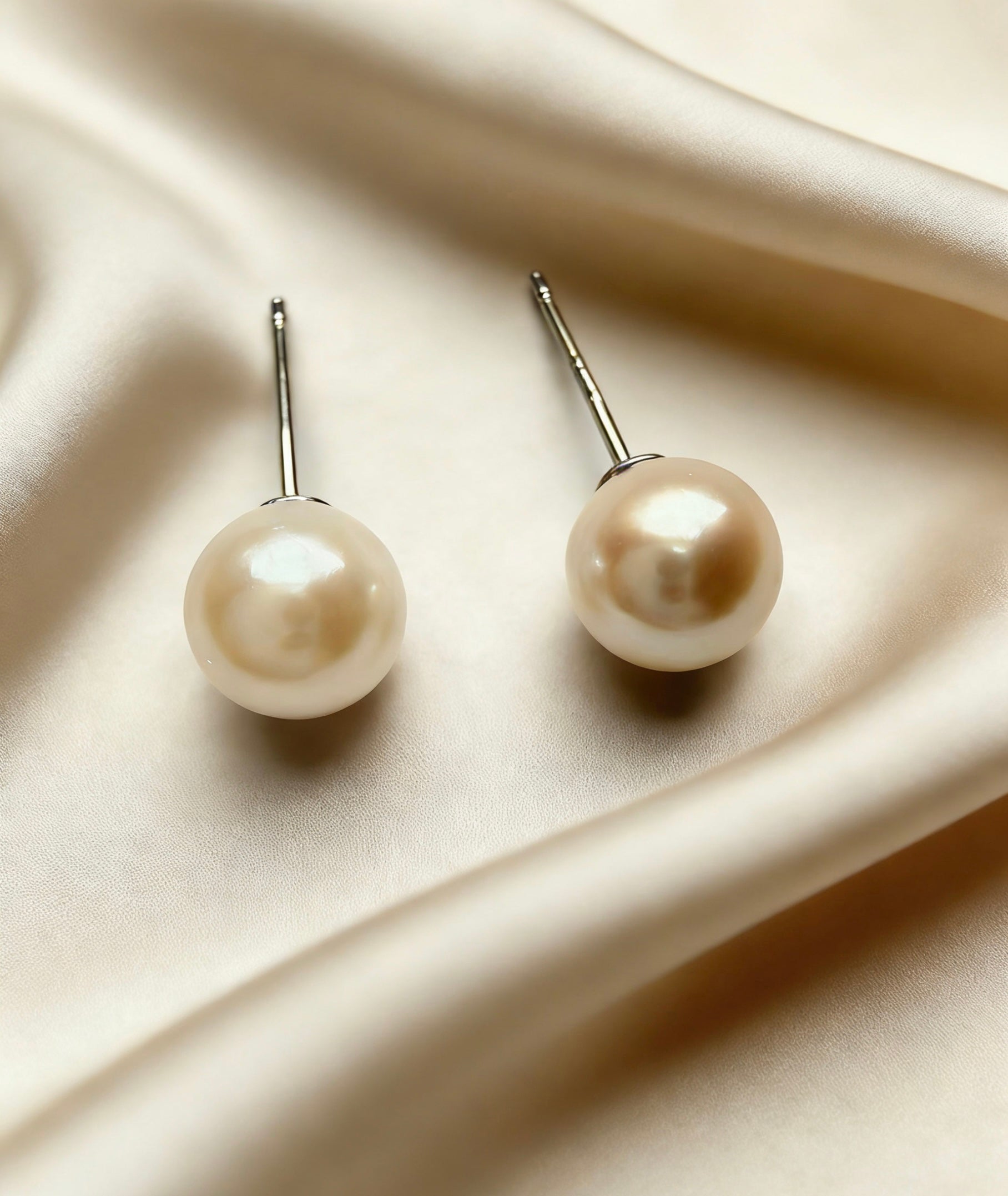 7mm round South Sea pearl stud earrings with 925 sterling silver posts on a soft champagne silk background.
