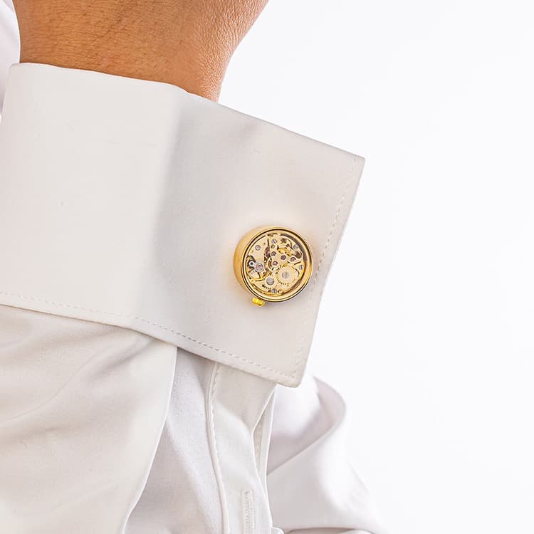 Gold brass skeleton movement cufflinks with visible gears and ruby bearings worn on a crisp white dress shirt cuff.