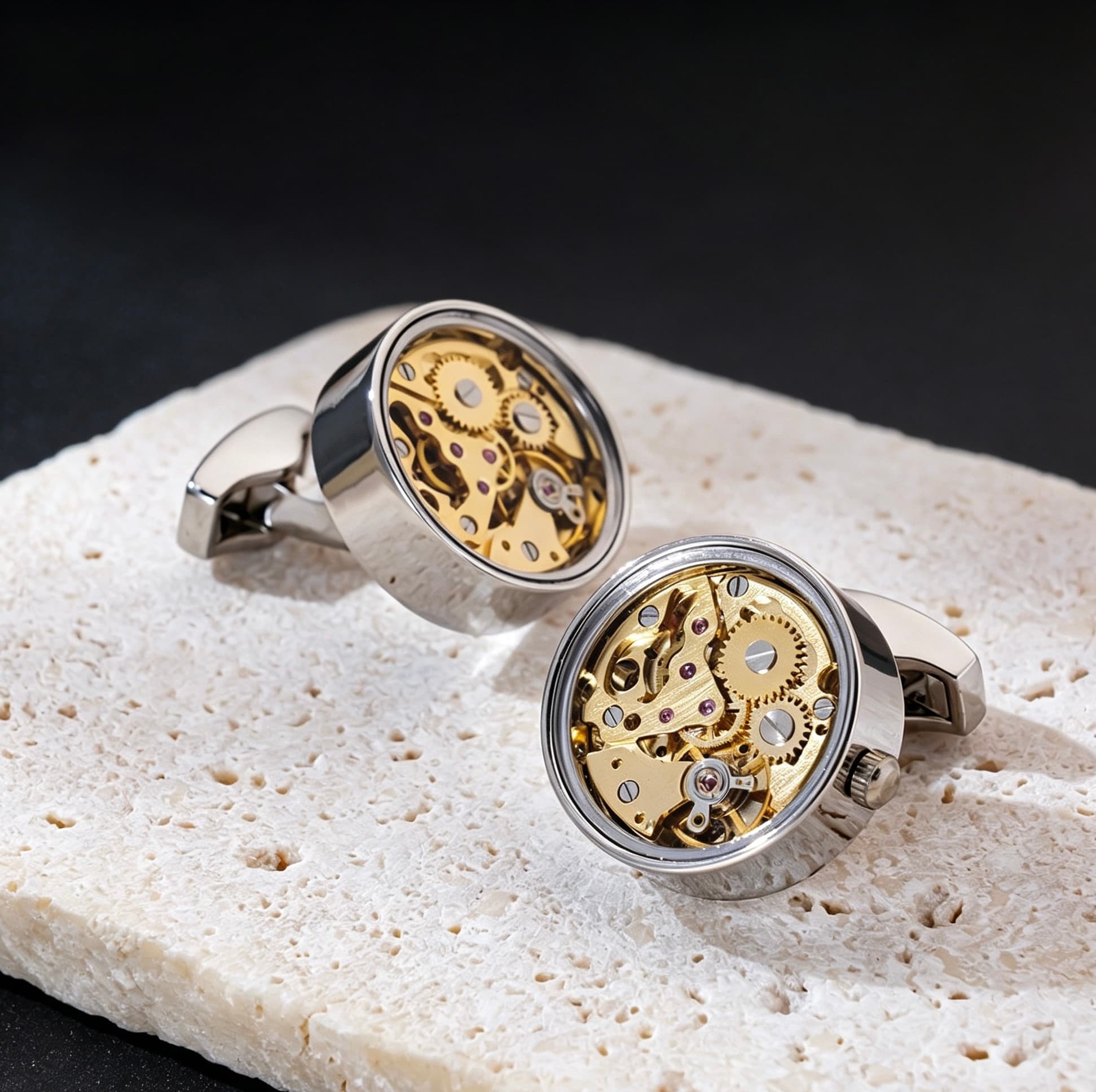 Round brass skeleton movement cufflinks with visible gold gears and ruby bearings on a textured stone surface.