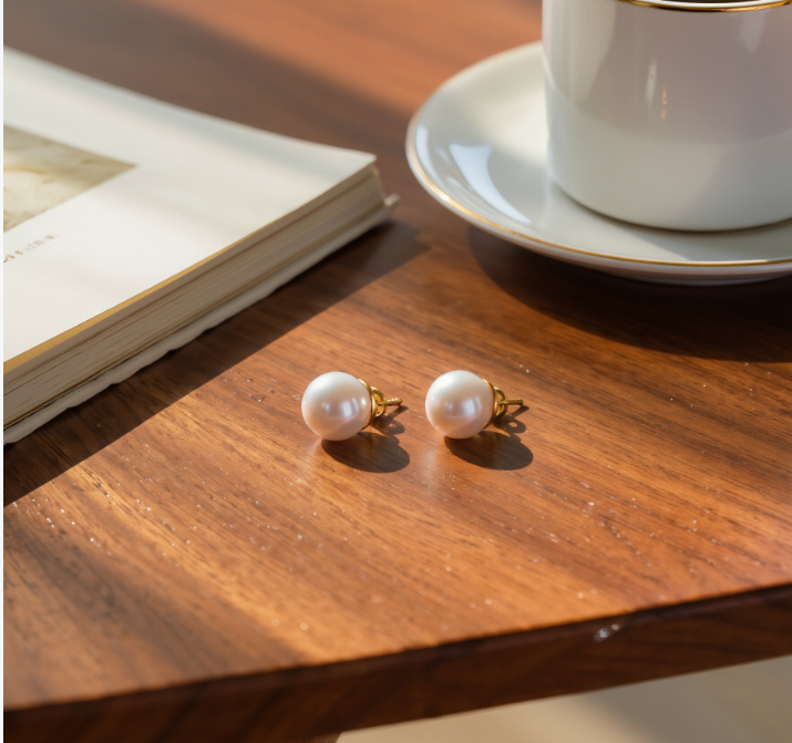 7mm white freshwater pearl stud earrings with gold-tone posts resting on a wooden table.
