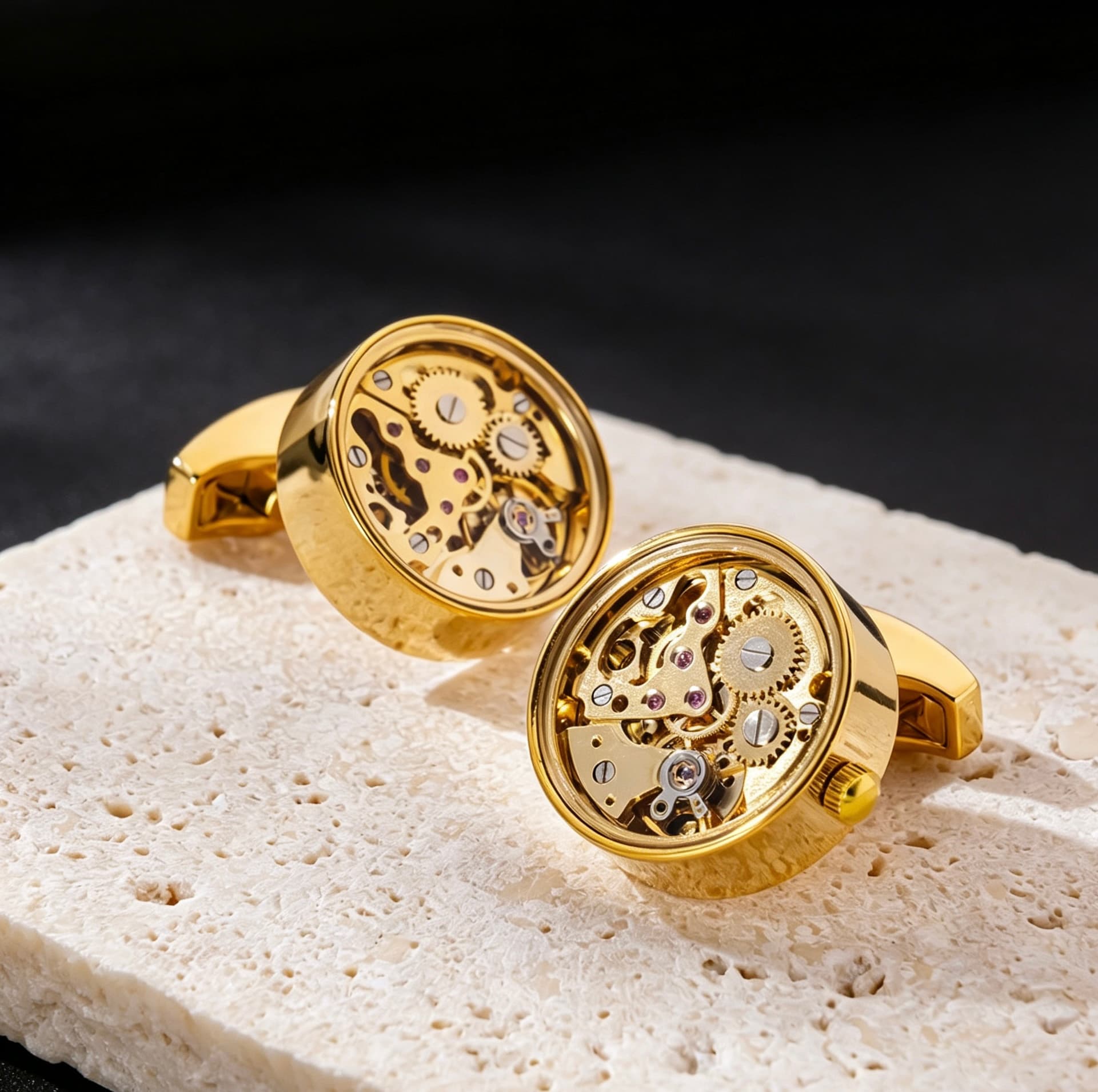 Gold brass skeleton movement cufflinks with visible gears and ruby bearings on a textured stone surface.
