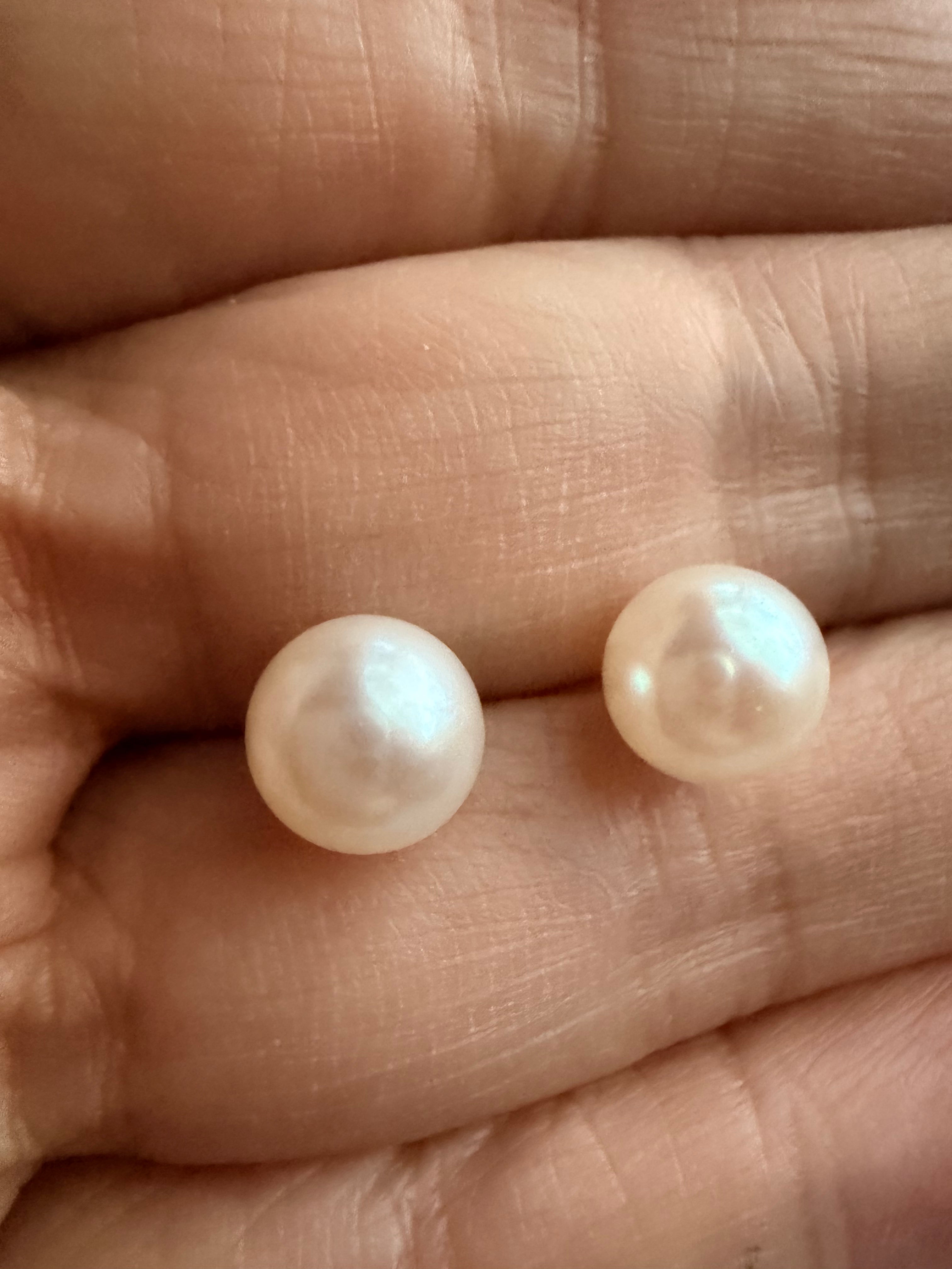 Pair of 7mm white freshwater pearl stud earrings with a soft luster held in a palm.