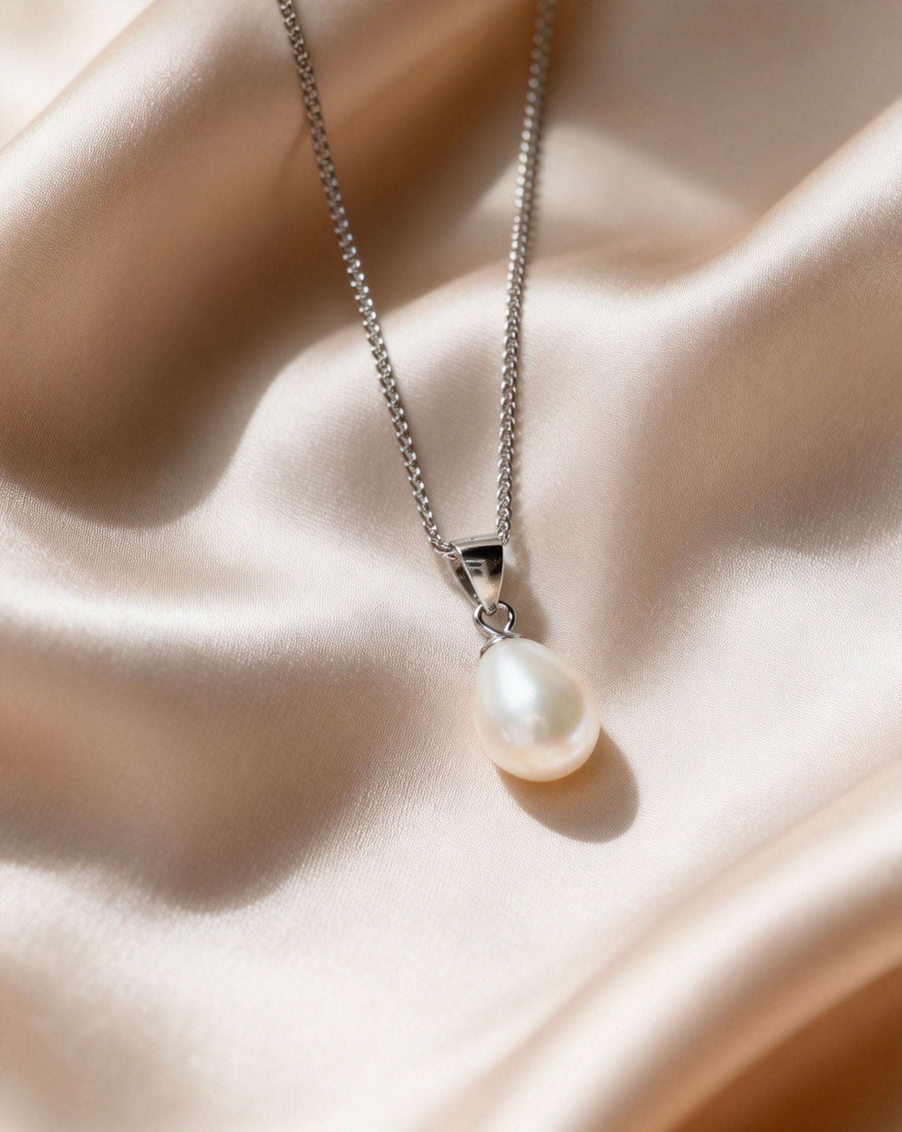 Baroque freshwater pearl pendant on a delicate 925 sterling silver chain resting on champagne-colored satin fabric.