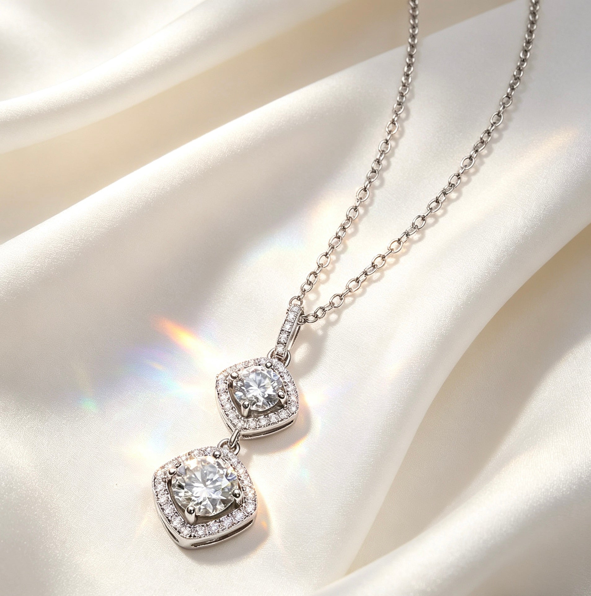 Double moissanite pendant necklace with two round D-color stones in a silver-toned halo setting on white silk.