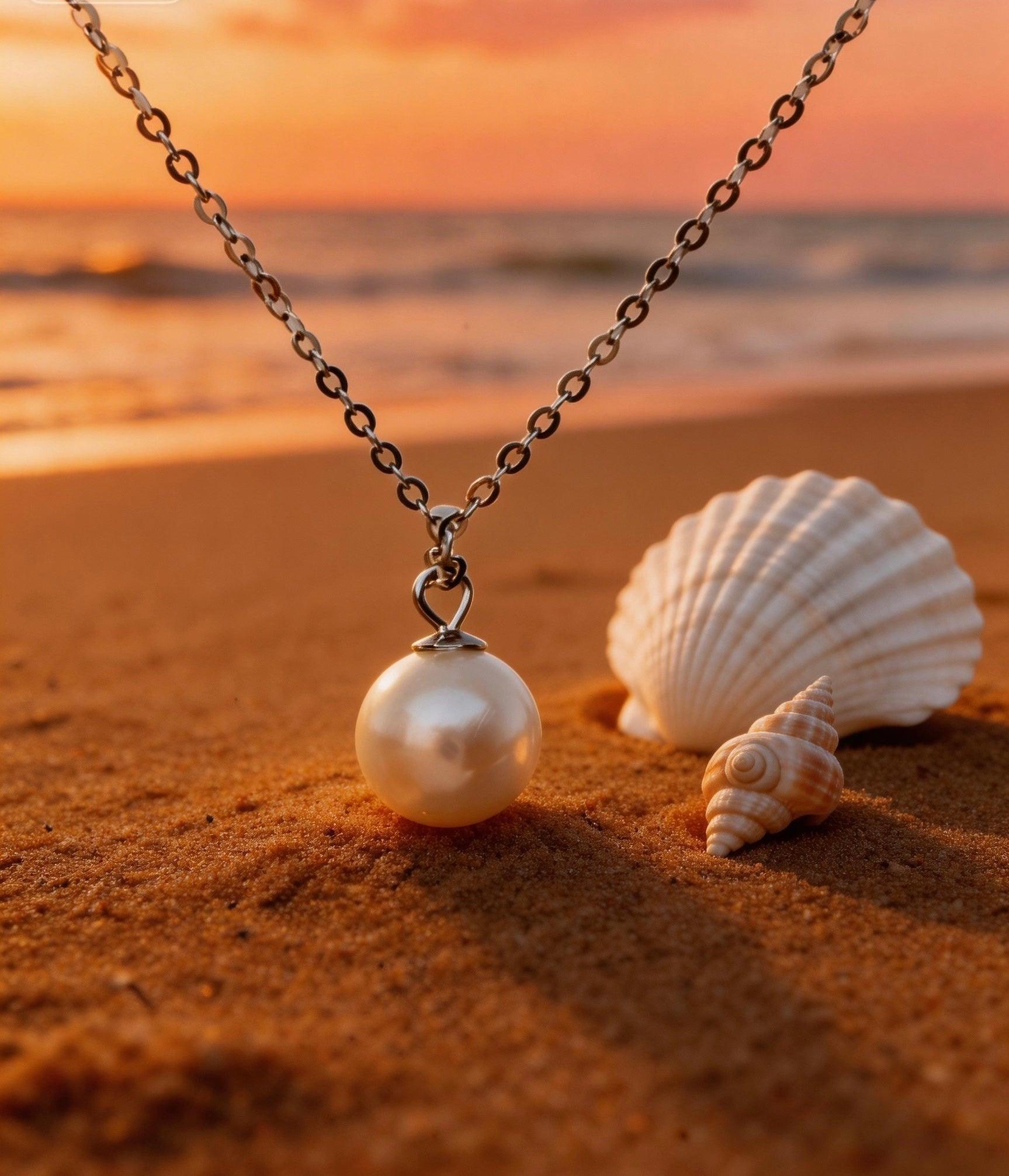 7mm Hepu saltwater pearl pendant on a silver chain resting on a sandy beach at sunset with seashells.